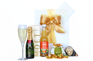 Small white gift box with gold ribbon and bow, packed with 200ml Mini Moët, Phoenix orange juice, pretzel mix and pistachios 